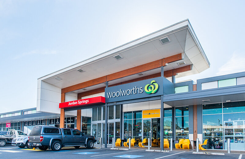 Exterior view of Jordan Springs Shopping Centre showcasing the Woolworths signage, large glass entry, and landscaped pedestrian access.