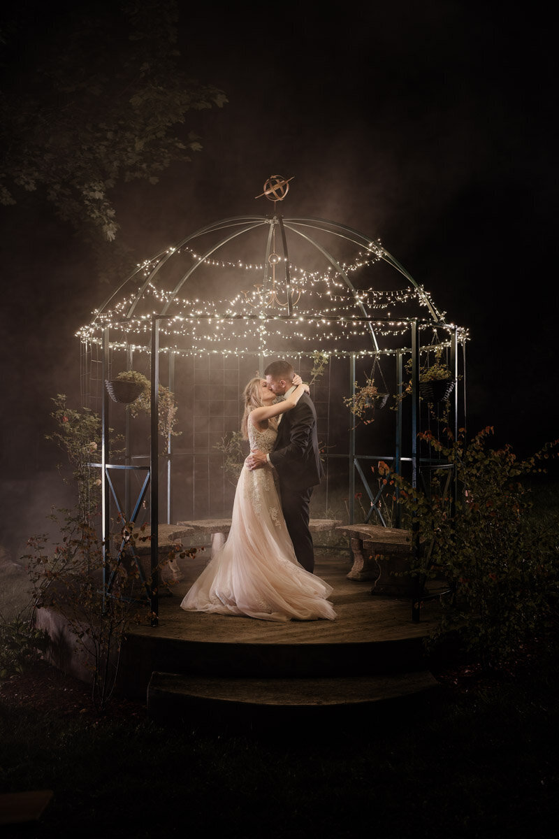 Photo de mariage en Haute-Savoie : les mariés s’enlacent sous un kiosque illuminée, dans une ambiance nocturne féérique.