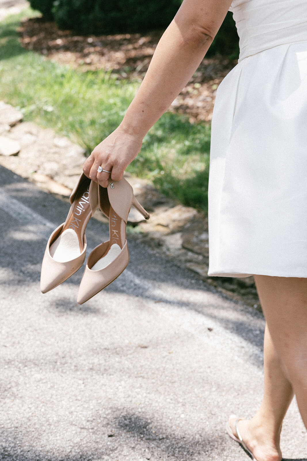 Bride holds her wedding beige wedding shoes while walking to her elopement ceremony location.