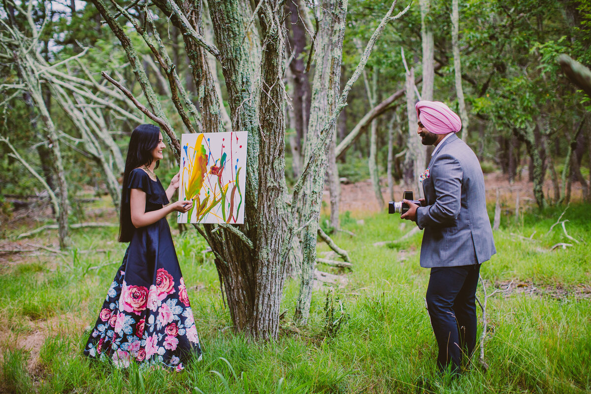 A sikh couple in a forest painting and taking a picture with a film camera expressing their hobbies during their engagement session