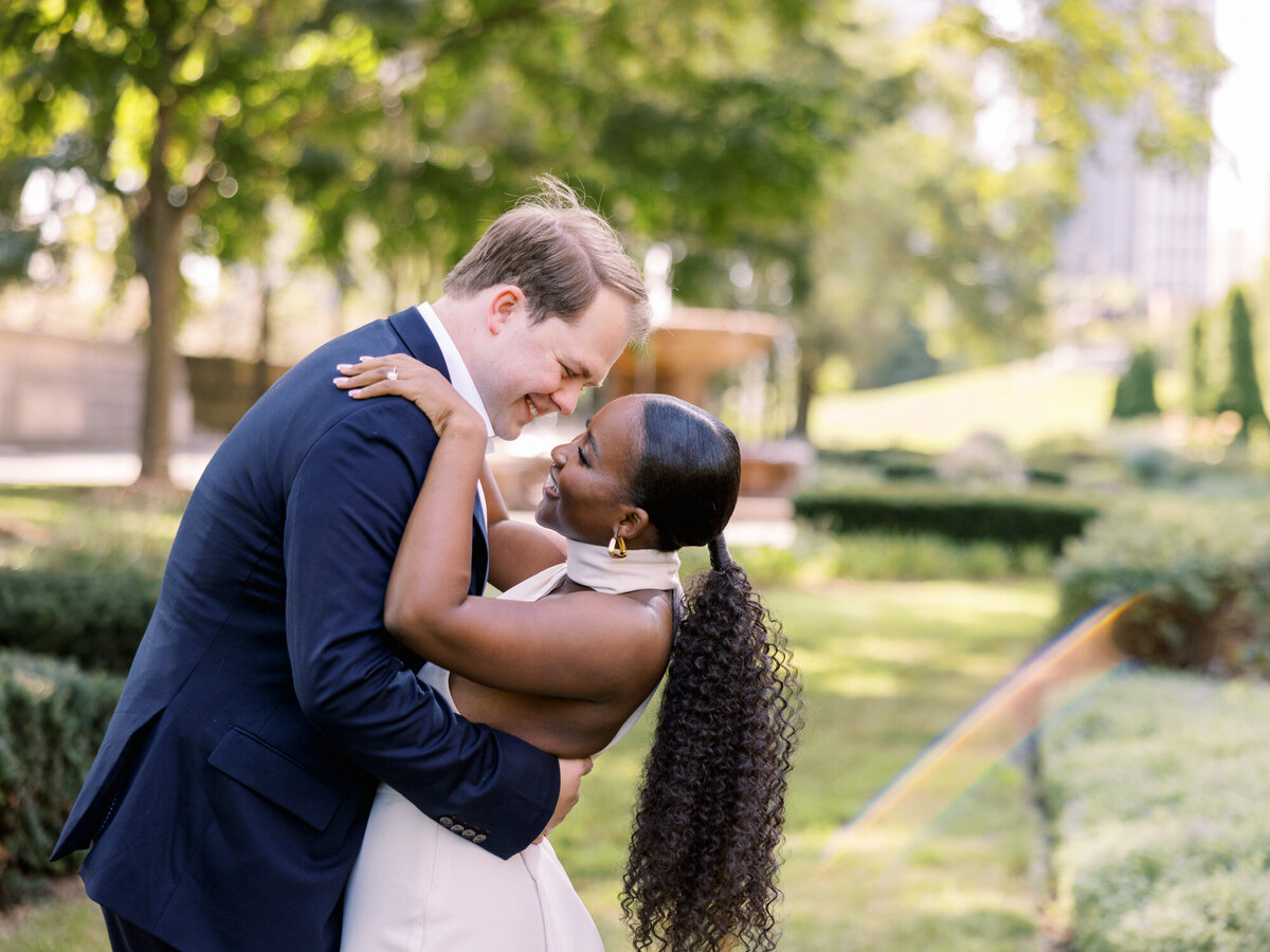 A couple shares a romantic moment in a formal garden along Michigan Avenue, surrounded by lush greenery and city charm.