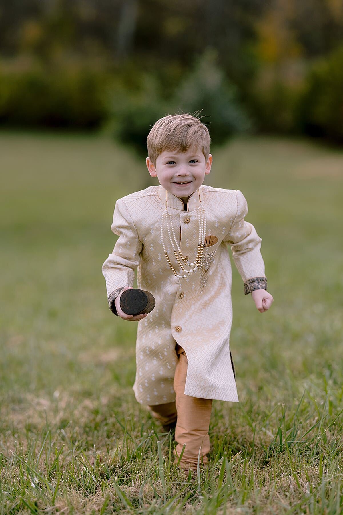 Ring bearer wearing an ivory and beige sherwani at a Nashville Indian wedding as he runs down the aisle at Ravenswood Mansion.