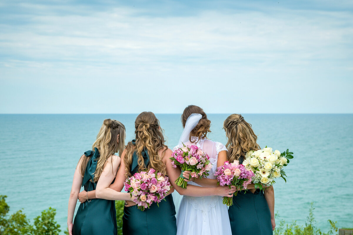 Bridesmaids with bouquets looking over lake Erie.