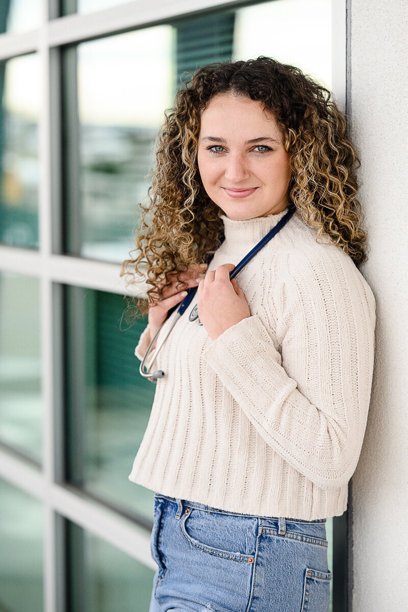 A Denver commercial photographer and branding photographer takes a picture of a nurse holding her stethoscope in a white sweater and jeans for her branding photos and branding session.