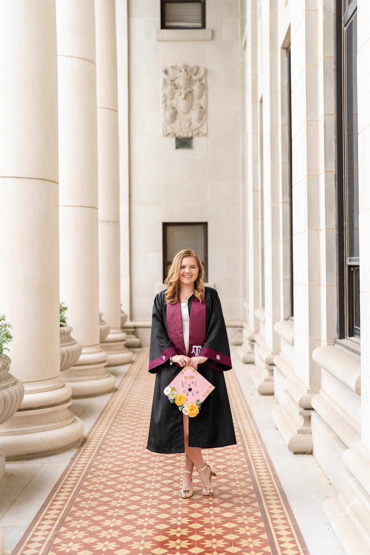 Texas A&M senior girl wearing gown and Aggie stole while holding decorated grad cap in the columns of the Administration Building