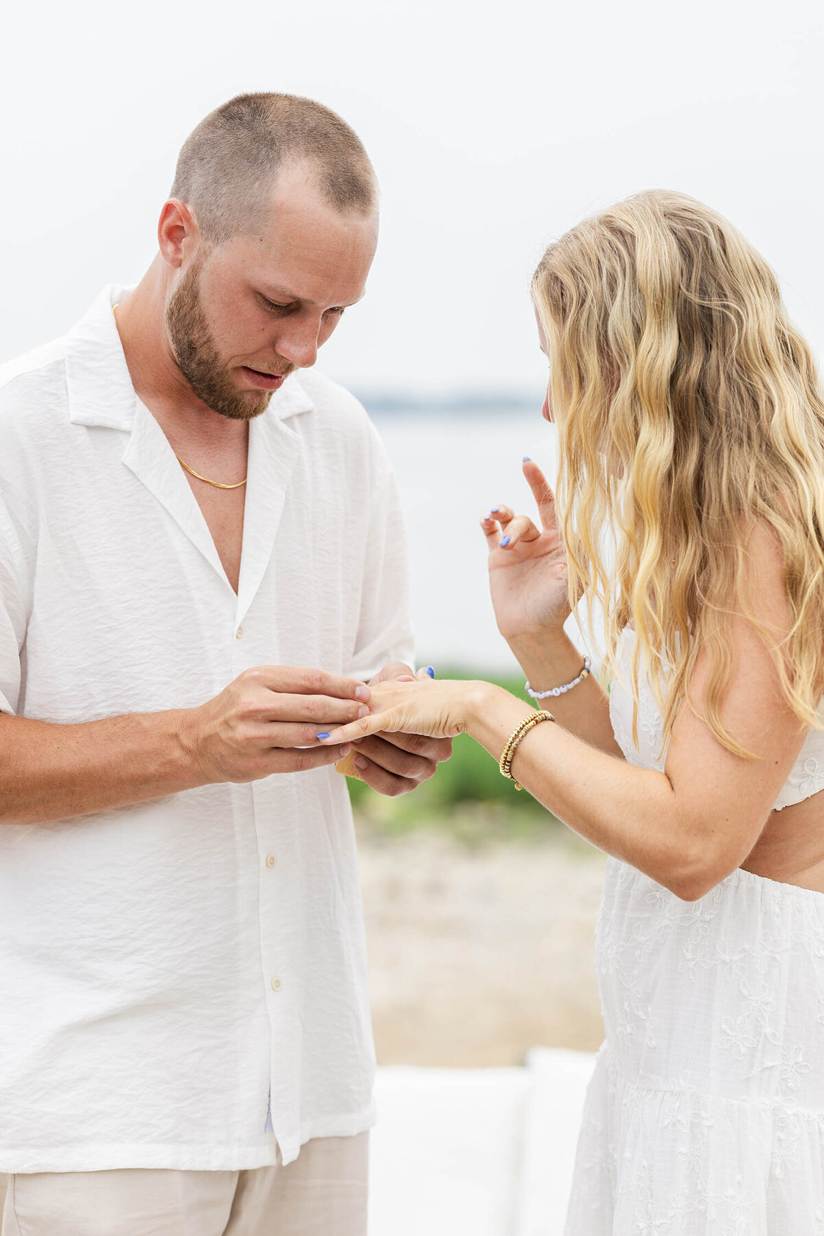 A man wearing a cream white shirt is putting a ring on a woman's finger during a Coastal Connecticut engagement session