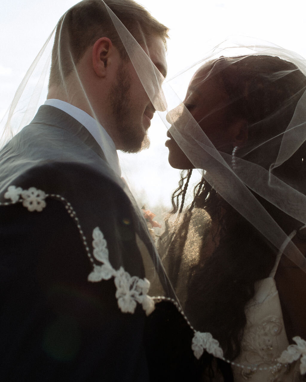 Tender moment between bride and groom as they kiss beneath her flowing veil, capturing the beauty and romance of their Christ-centered celebration.
