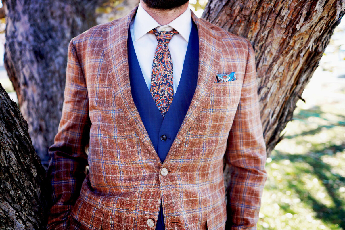 A groom has a close up moment to highlight his stylish plaid suit and tie with navy vest,