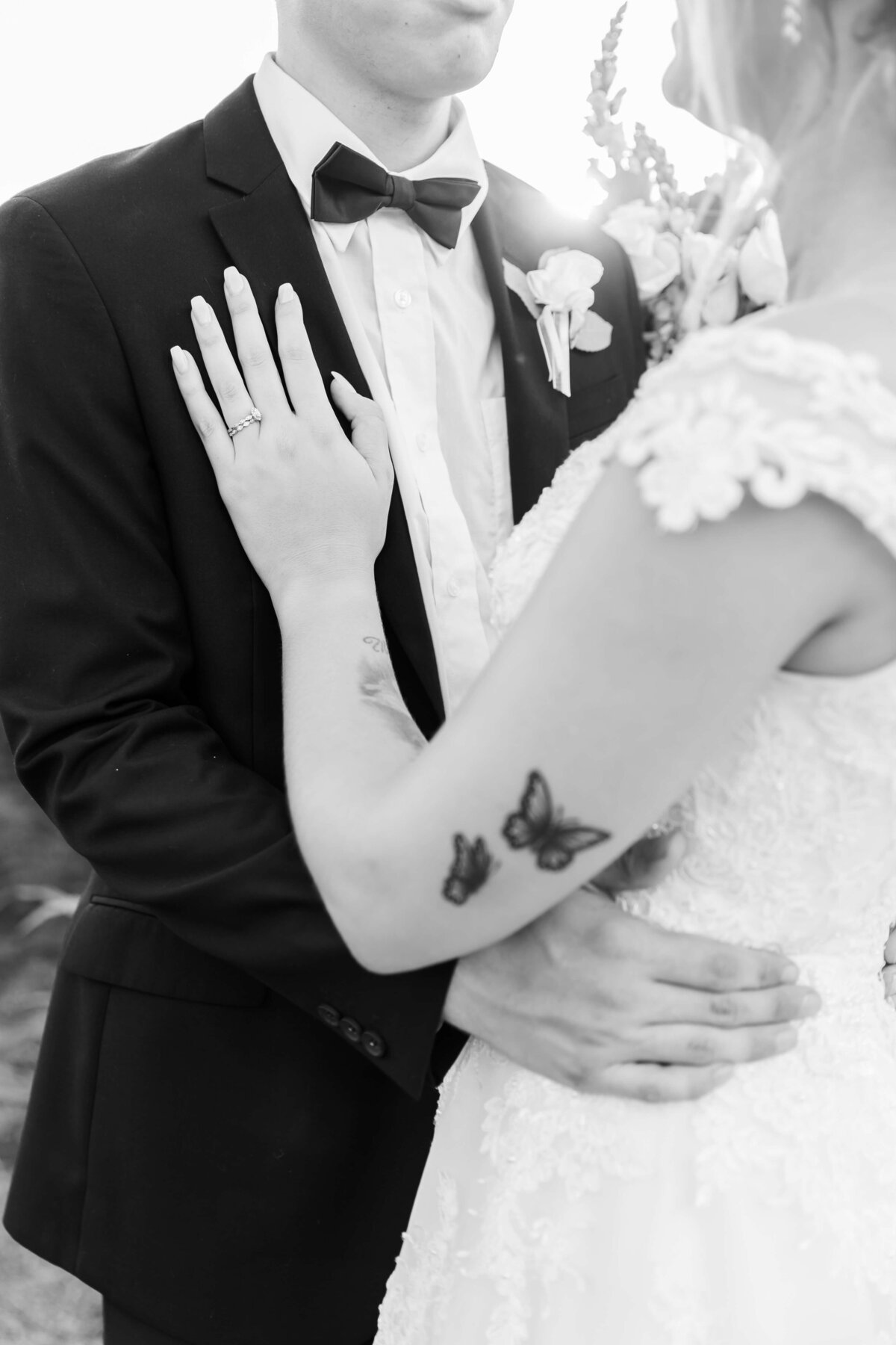 Bride and groom embracing, bride with butterfly tattoos on her arm