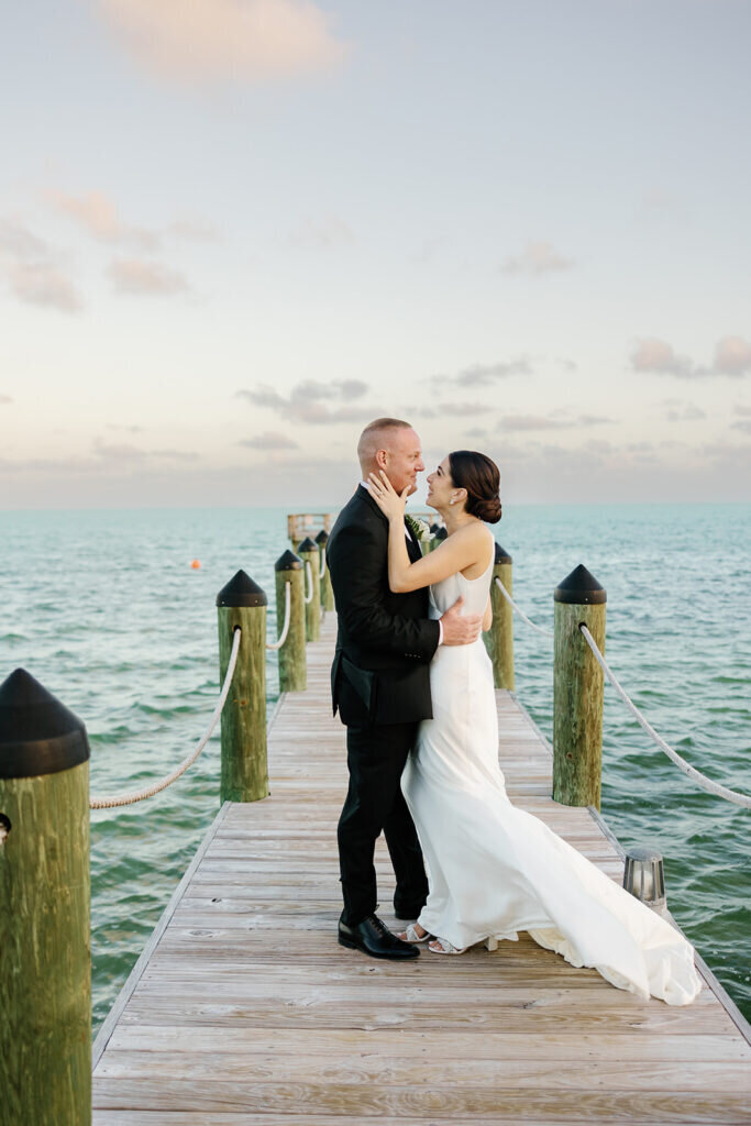 A timeless portrait of the newlyweds embracing on a dock over the ocean, with soft waves and a golden sunset setting the perfect scene. Destination wedding photography by Claudia Amalia Photography in the Florida Keys.