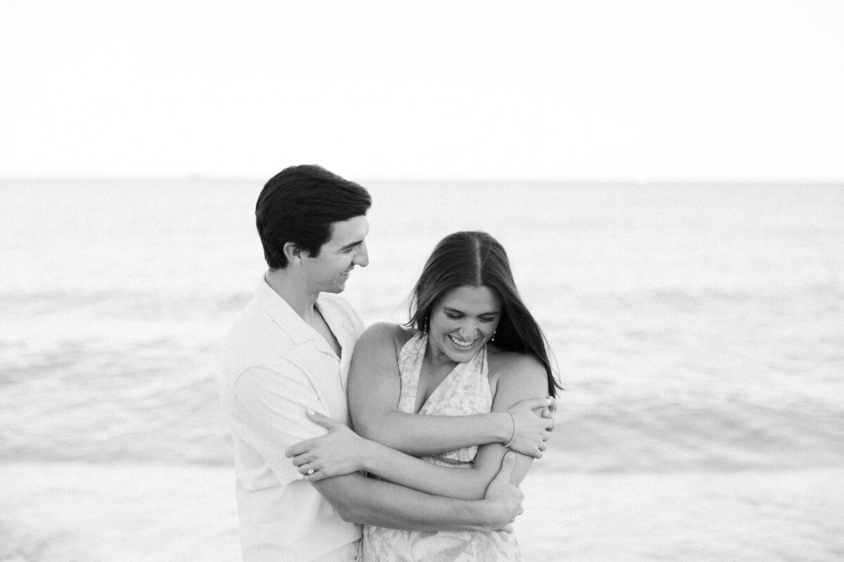 Rebecca and Graysen share a joyful embrace on the sandy beach at Marriott Hotel Fort Lauderdale, captured in a romantic black and white engagement portrait by Claudia Amalia Photography.