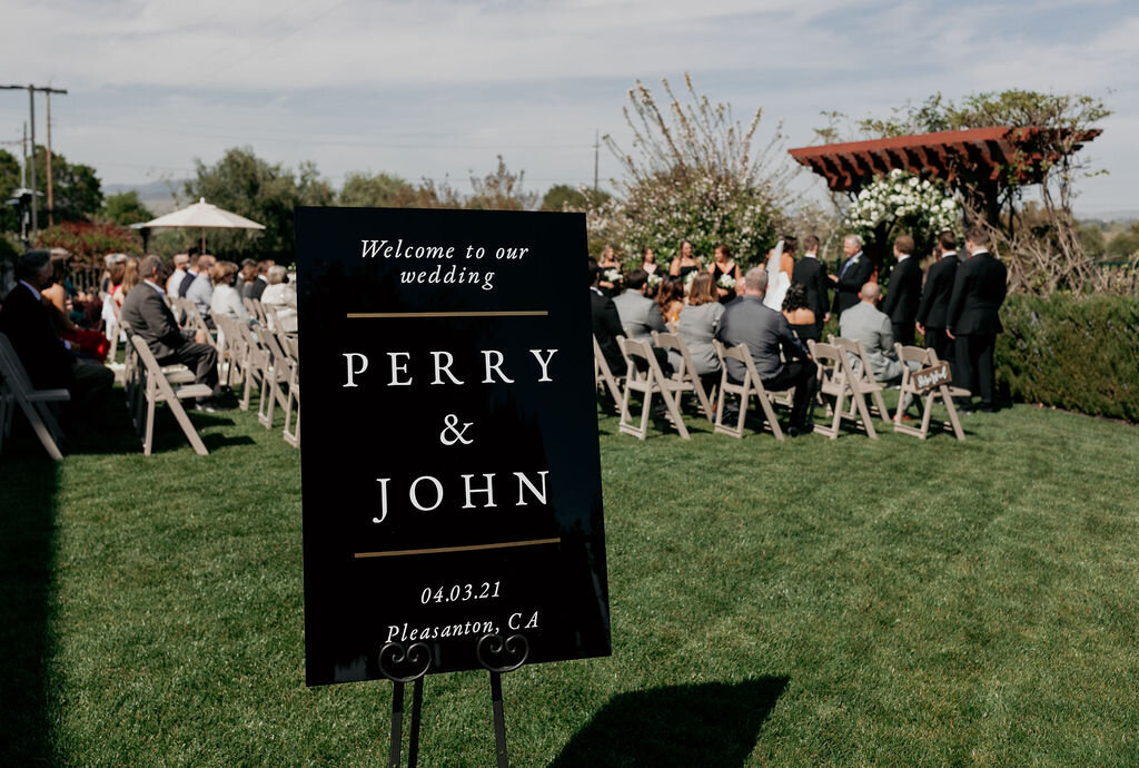 Black acrylic welcome sign on a black easel at the ceremony site of a spring wedding at the Palm Event Center in Pleasanton, CA.