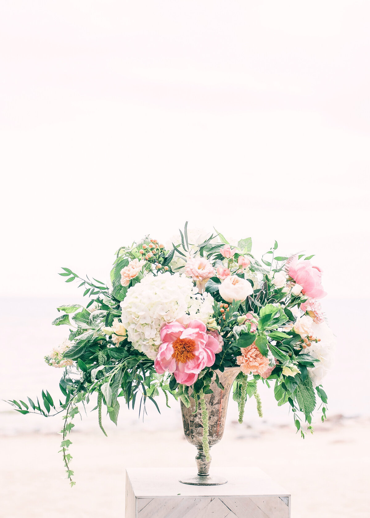 A beautiful floral centrepiece with pink peonies  and white hydrangeas fills a rustic vase on a beach. background