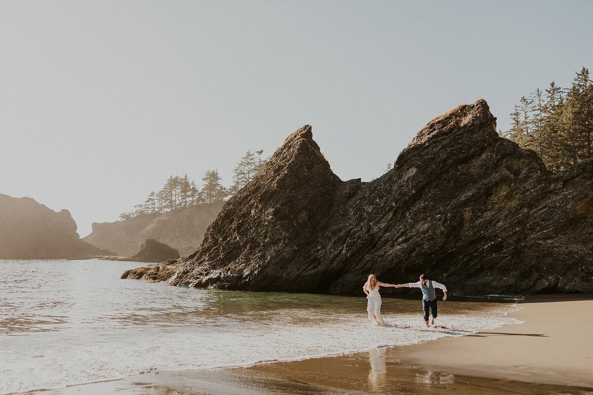 A couple in wedding attire running on an Oregon Coast beach during their elopement