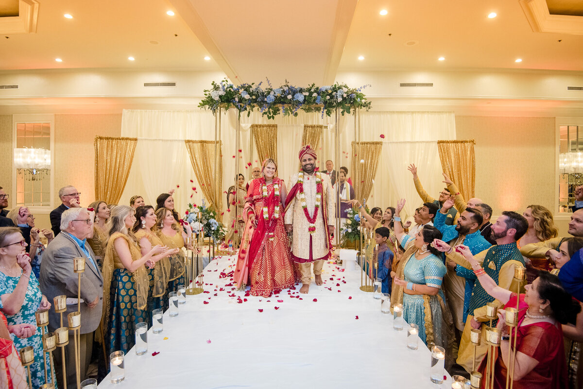 Beautiful Indian wedding ceremony at Le Méridien Charlotte with bride and groom walking down the aisle under the mandap as guests shower them with rose petals, captured by a top Indian wedding photographer in Charlotte.