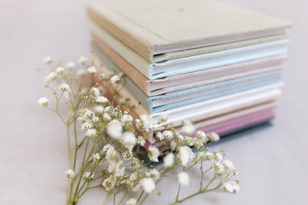 A stack of the photo albums available for purchase through Justine Renee Photography. A twig of baby's breath is in front of them.