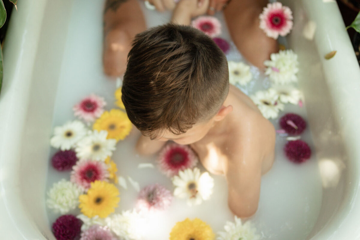 Child sitting in a milk bath surrounded by colorful flowers