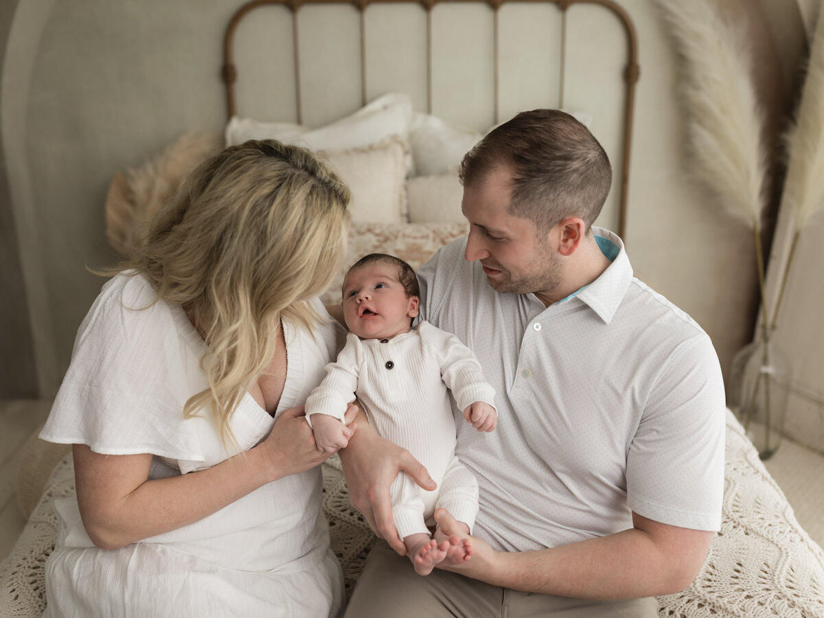 mom and dad holding newborn baby boy in white onesie for studio lifestyle session cleveland newborn photographer
