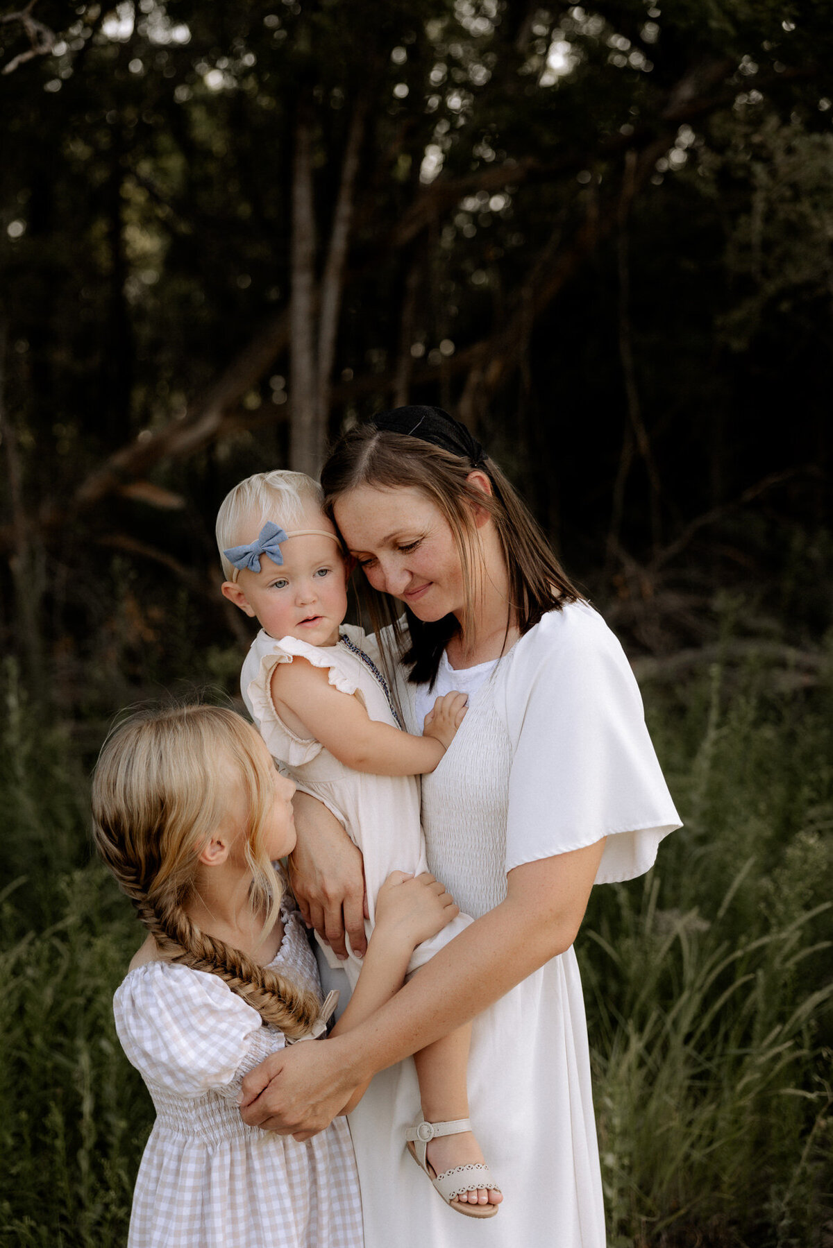 momma holding her little one on her hip while lightly touching the chin of her older daugher. Lubbock family photographer Mary Wiebe captured this gorgeous image.