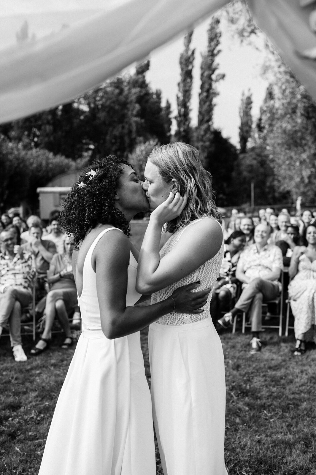 Twee bruiden geven elkaar tijdens de ceremonie een kus voor hun gasten