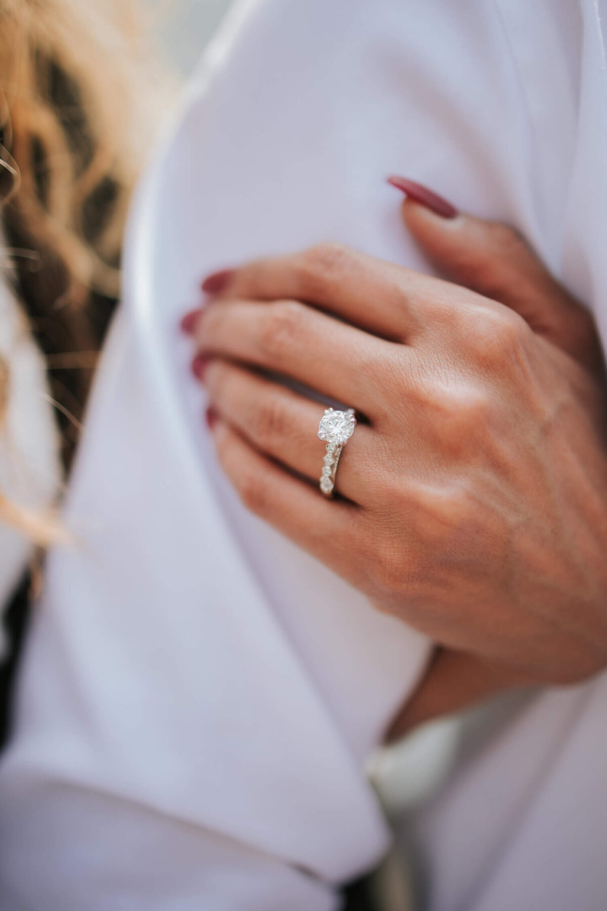 A close-up of a woman's hand adorned with a sparkling diamond engagement ring, gently resting on her partner's arm