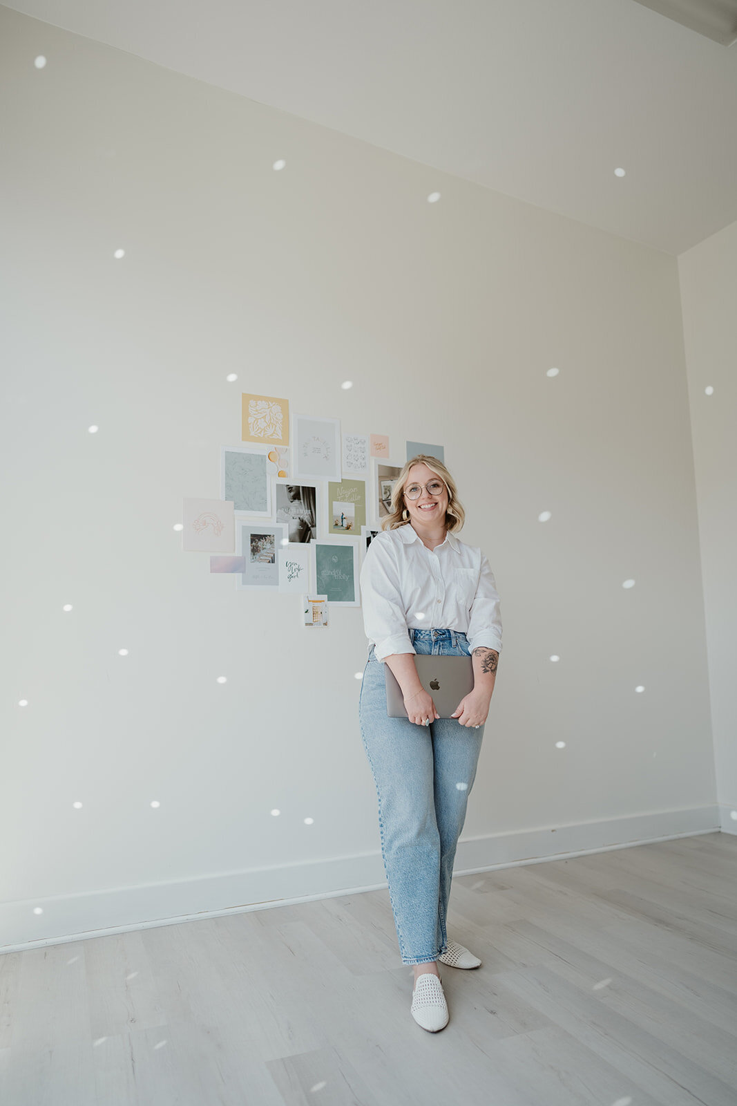Portrait of a woman holding a laptop while standing by a mood board wall during a Wildher and Co studio branding session.