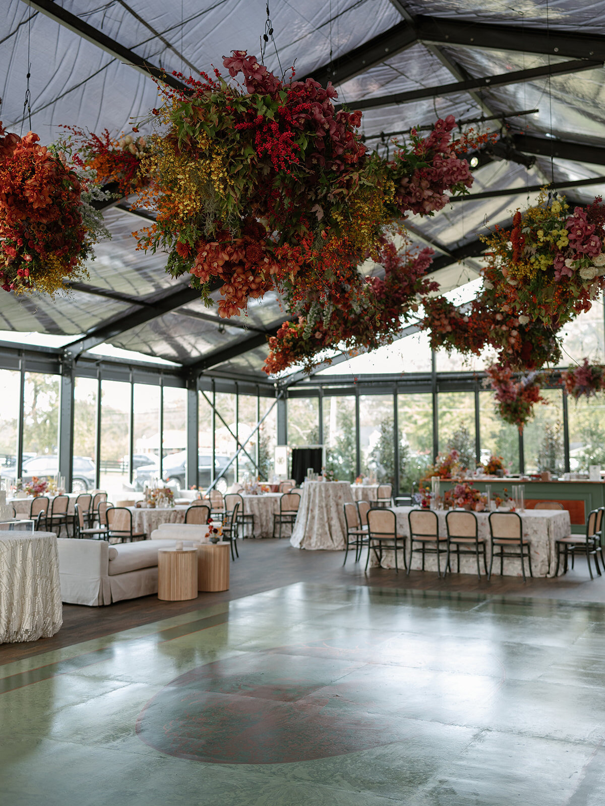 Interacting and sculptural floral clouds hang over the dance floor and bars of this fall wedding reception in Tennessee. Clear top tent build out for fall wedding reception in Tennessee hills.  Product clustered floral clouds in a tasteful fall color palette of copper, ruby, gold, burgundy, rust, and lavender. Orchids, bittersweet berries, butterfly ranunculus, and tulips are highlighted. Unique floral design with flower forward large scale installations. Design by Rosemary & Finch Floral Design in Nashville, TN.