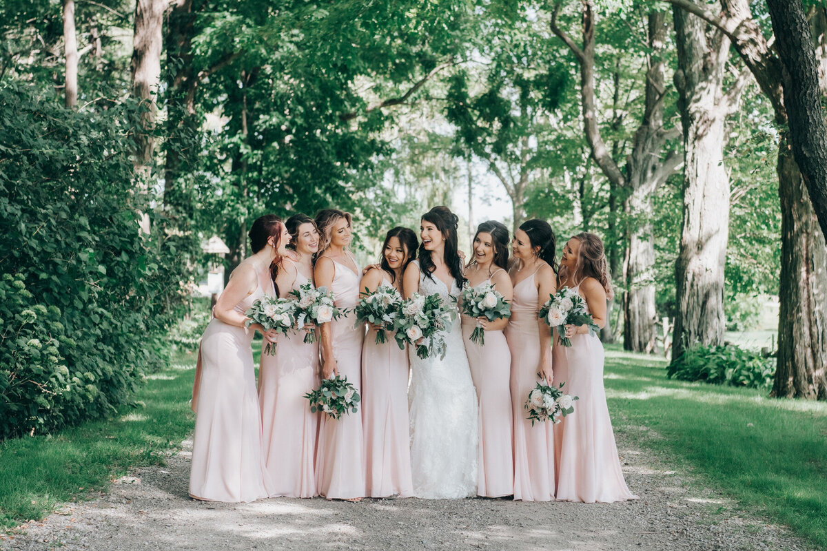 Bride posing with bridesmaids wearing pink bridesmaids dresses in a whimsical forest on a Summer wedding day at Wheatfield Estate