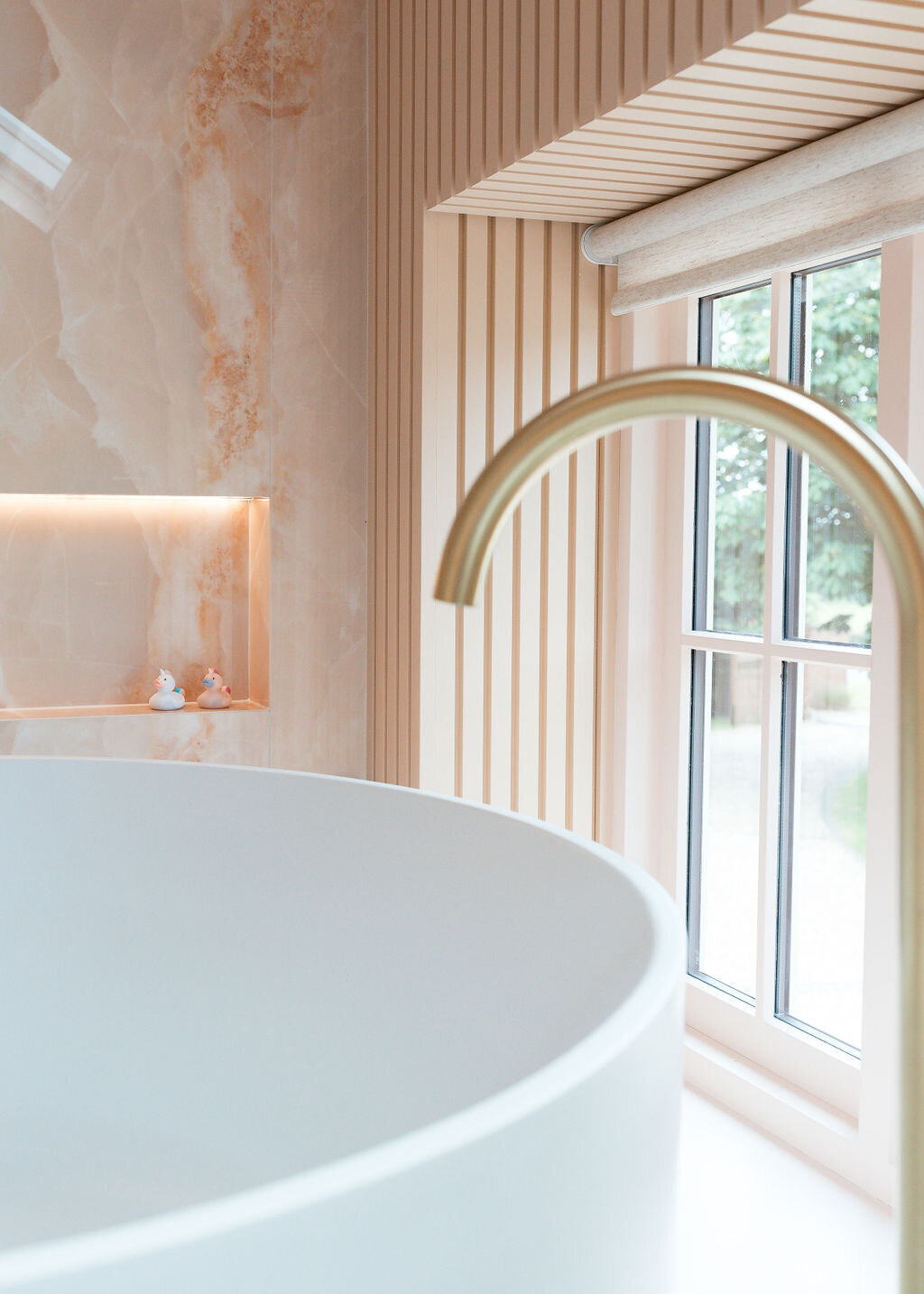 A close-up view of a round white bathtub, featuring a sleek gold faucet in a modern pink marble bathroom.