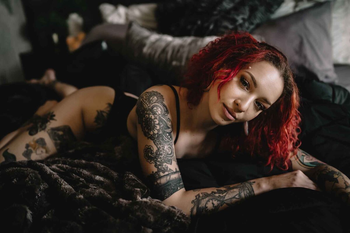 Tattoed-women-with-bright-red-hair-on-dark-bed