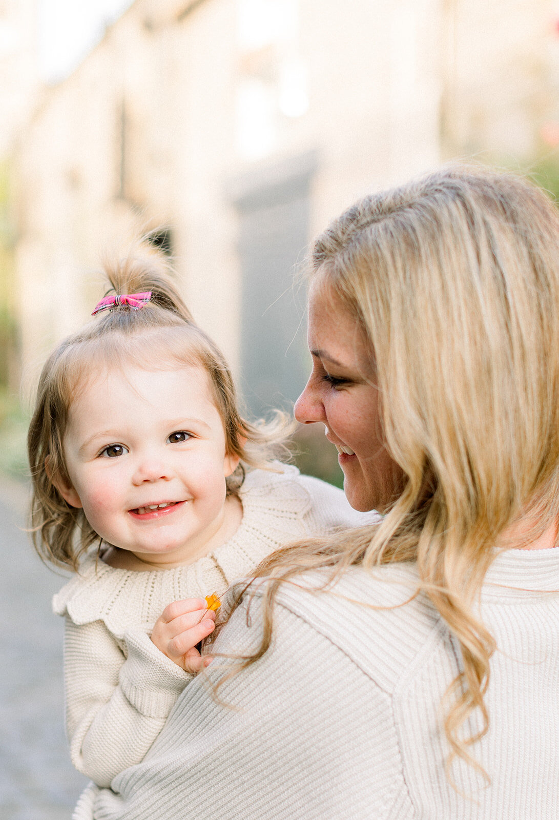 Small girl peeking around her mom to smile at camera