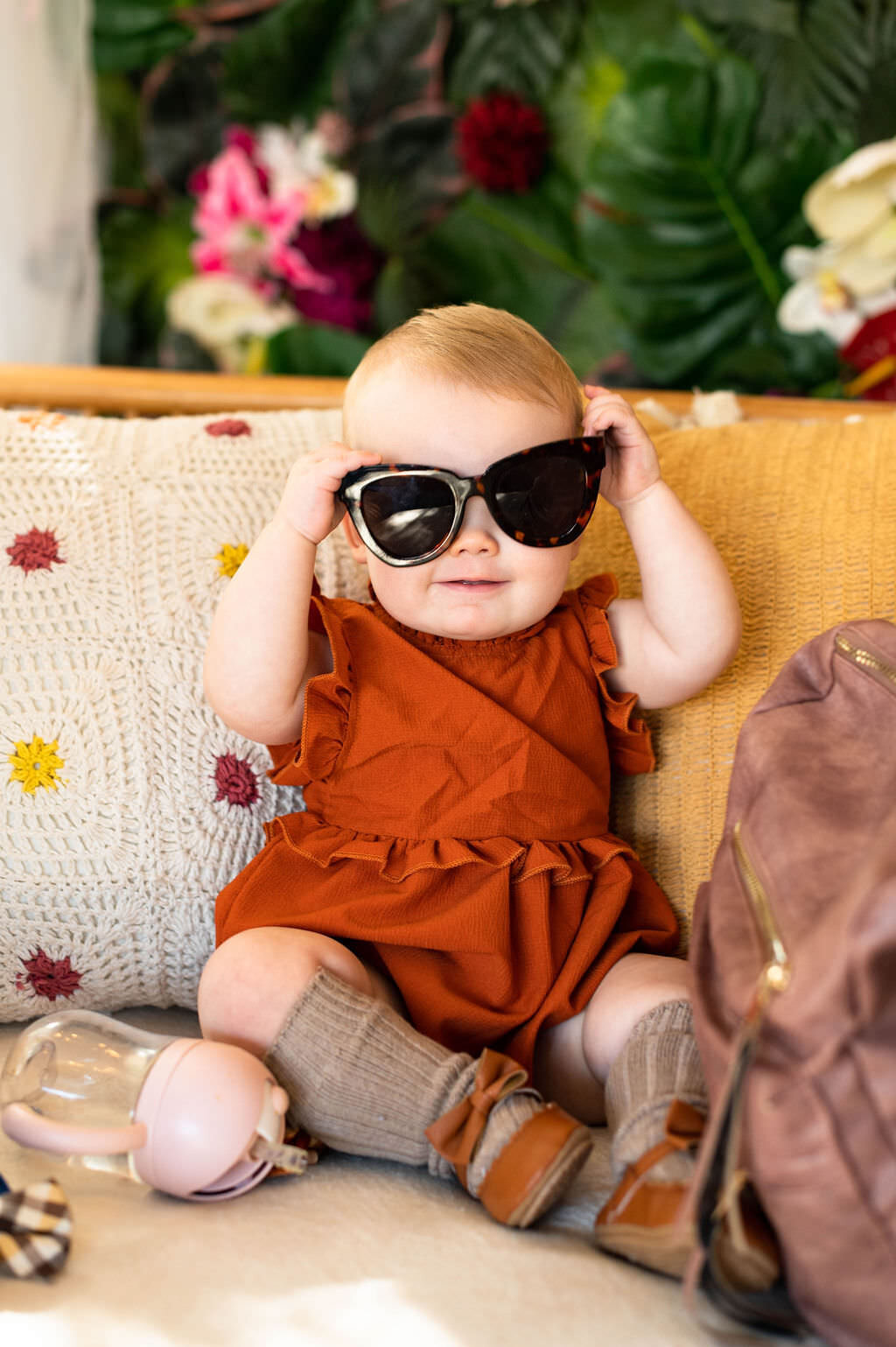 A baby sitting on a couch putting on sunglasses.