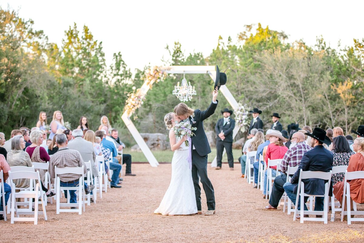 groom lifts his hat and kisses his bride in middle of aisle at La Dolce Vita in New Braunfels