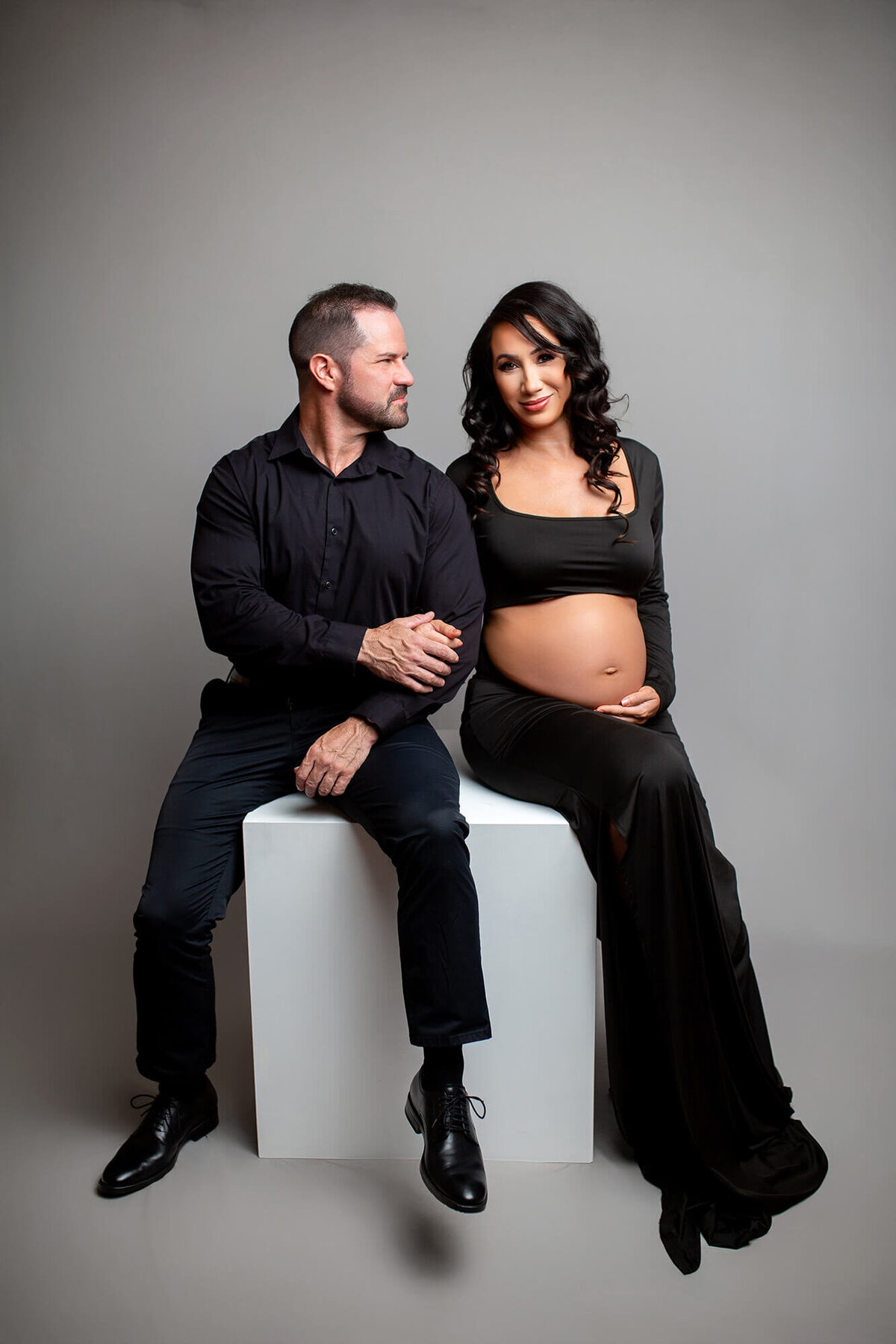 Husband and pregnant wife sitting on posing box with belly showing