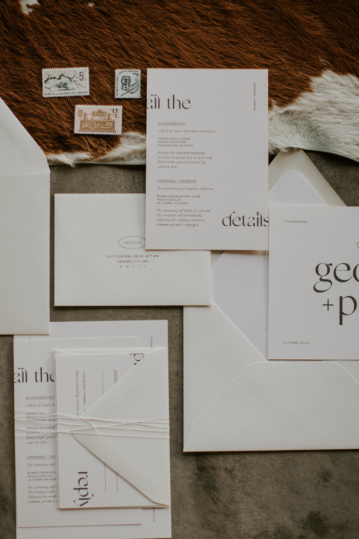 Mixed white wedding stationery with black font atop cow hide.