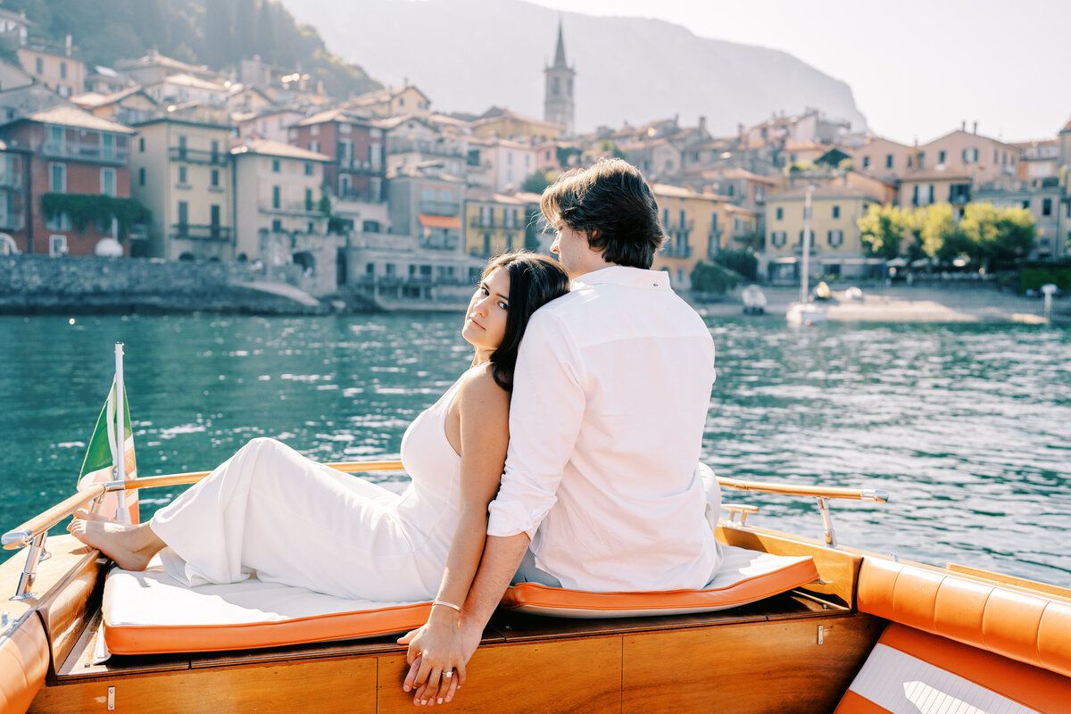 Couple on the back of a boat with Italy flag showing with the beautiful town of Varenna in the background photographed by Italy wedding photographer