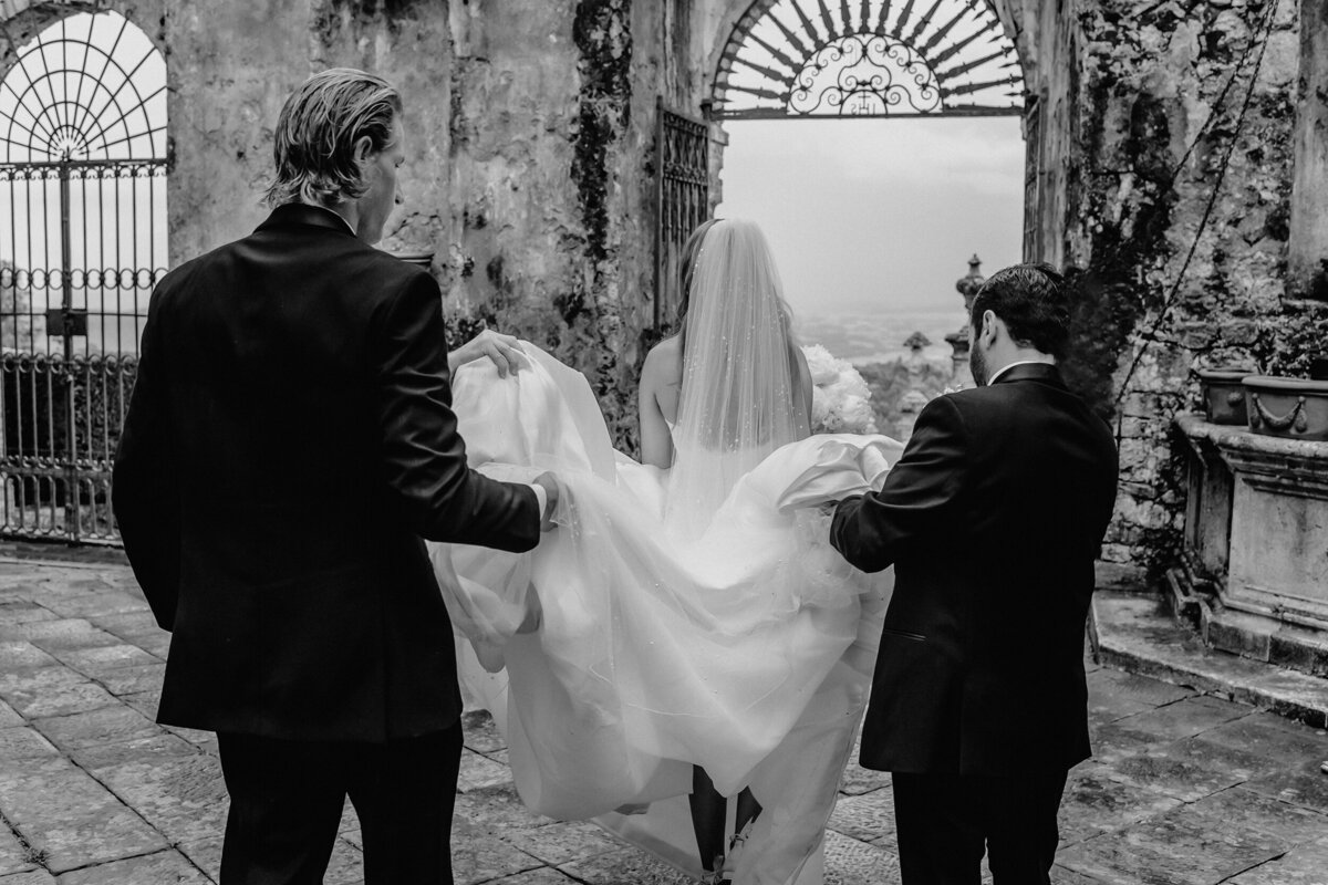 Groomsmen holding Brides dress as she walks in Castle