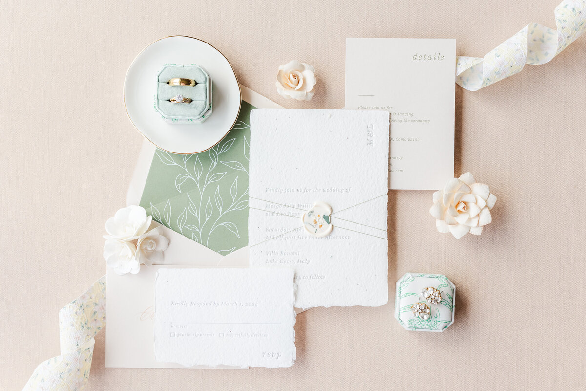 Wedding invitations and jewelry sit on a pink table