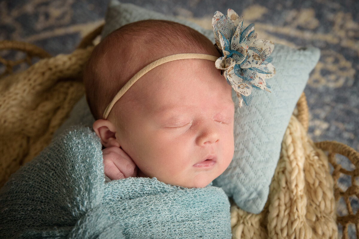 Newborn baby girl sleeping in light blue wrap with a cream and blue bow posed in a basket in her home in Green Bay, Wisconsin