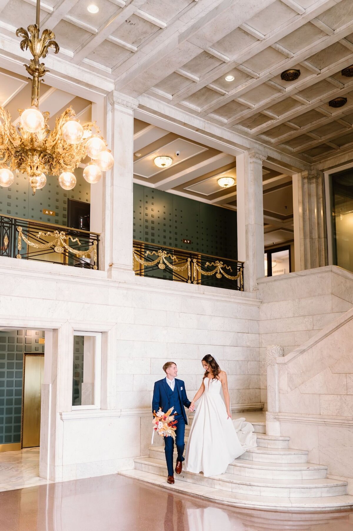 Groom leading his bride down a set of marble stairs