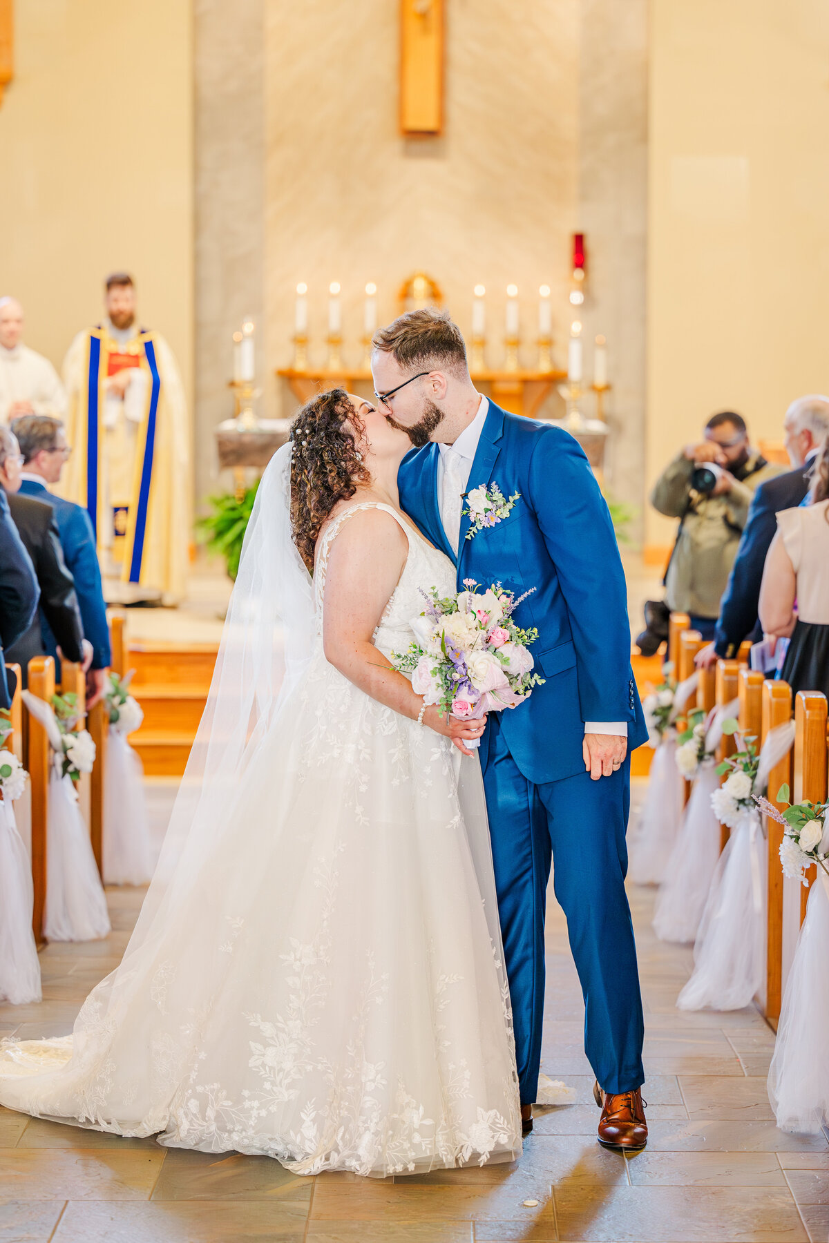 Bride and groom kissing halfway down the aisle after their catholic ceremony