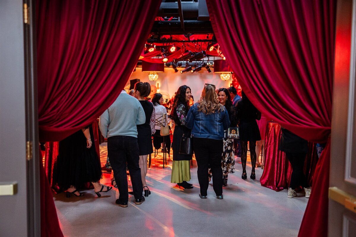 Large gathering at a Baroque-themed event, with guests dressed in formal attire mingling amid lavish decor including gilded furniture, crystal chandeliers, and rich drapery in a grand, ornately detailed space