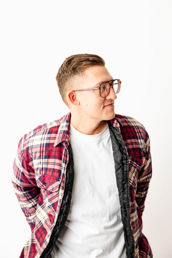 Man in red plaid shirt looks to side in white photos studio.