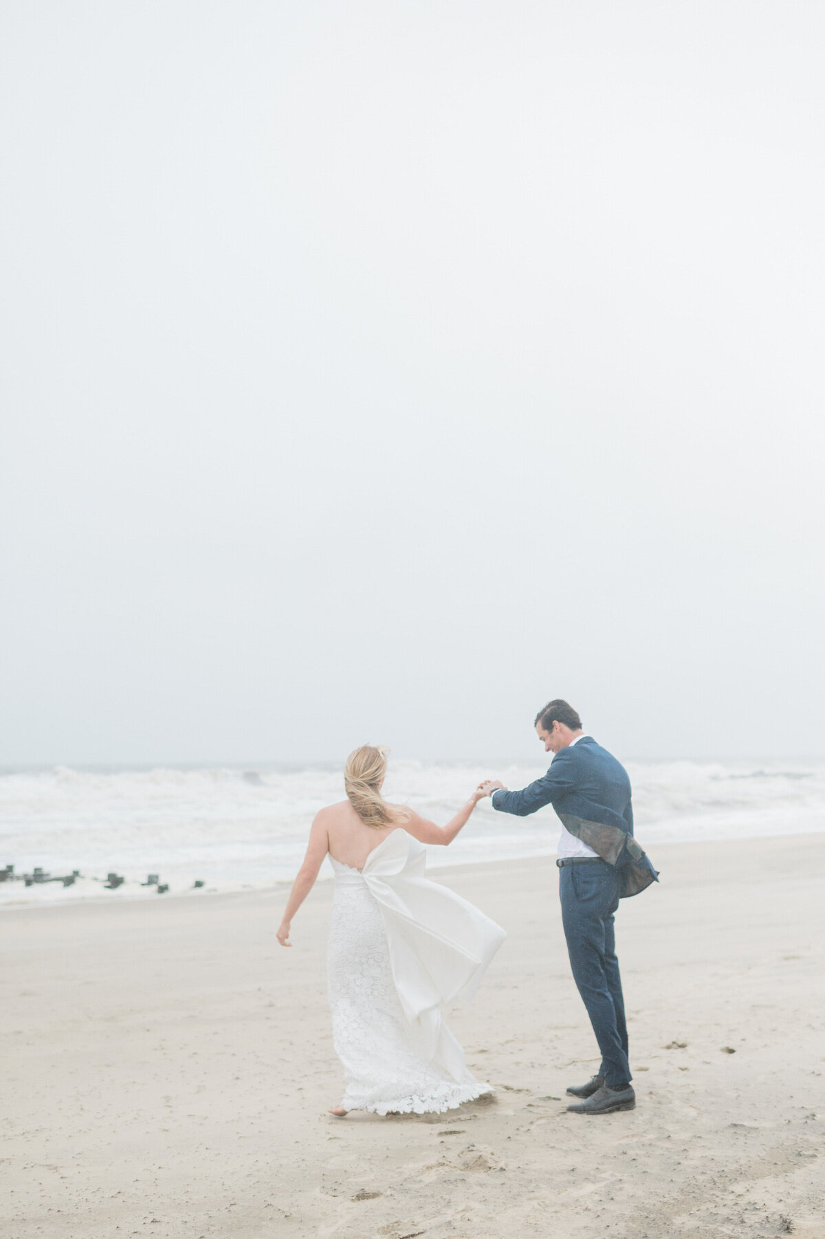 The groom twirls the bride with a happy expression as they dance barefoot in the sand