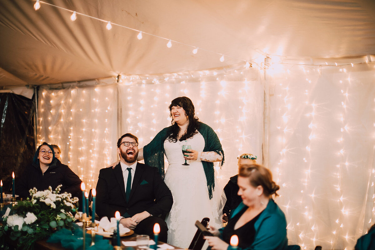 Bride and groom laugh during tented wedding reception
