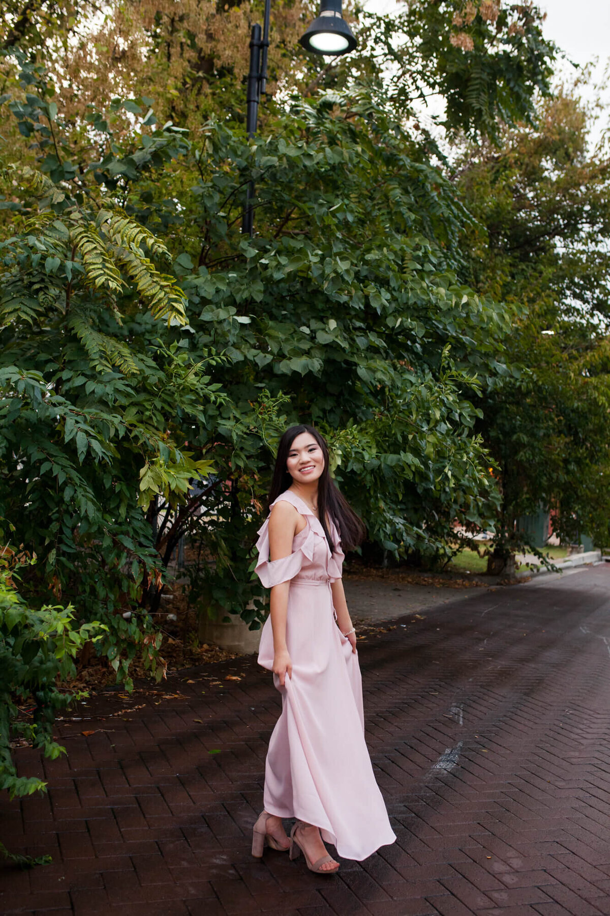 A lovely senior girl poses on a city side street surrounded by low hanging tree limbs. Captured by Springfield, MO senior photographer Dynae Levingston.