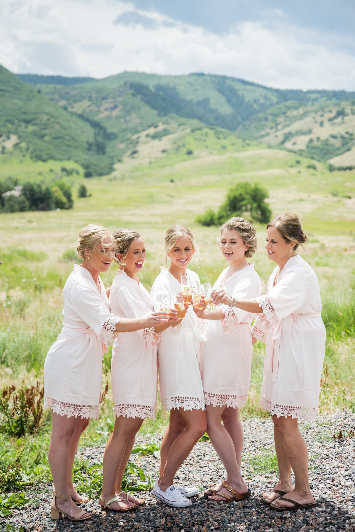 A bride and her bridesmaids dressed in robes share a toast of champagne with the Colorado landscape in the background at The Manor House.