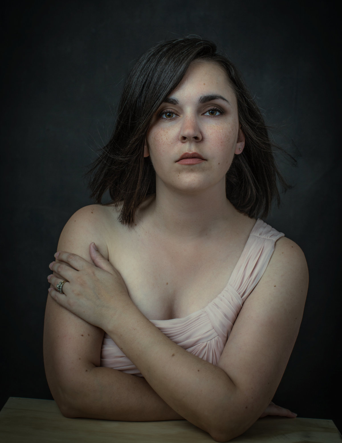 A woman with shoulder dark hair places her left hand on her right shoulder as she poses for a portrait photo at Janel Lee Photography studios in Cincinnati Ohio