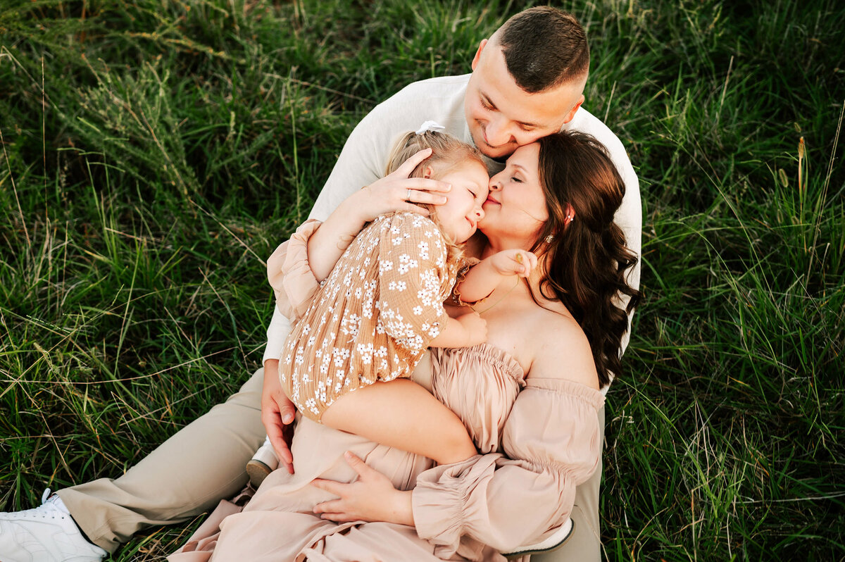 family cuddling holding pregnant baby bump in a field in Springfield MO during matenrity photography session