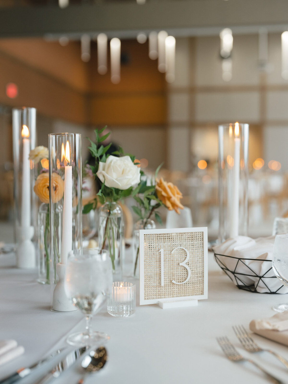 custom calligraphy rattan table numbers at a wedding reception table with florals and candles representing full service design and calligraphy by Life in Letters.